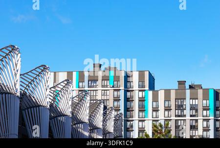 Immeubles résidentiels modernes avec des accents verticaux gris, blancs et turquoise, vus derrière des structures architecturales métalliques uniques sous un Banque D'Images