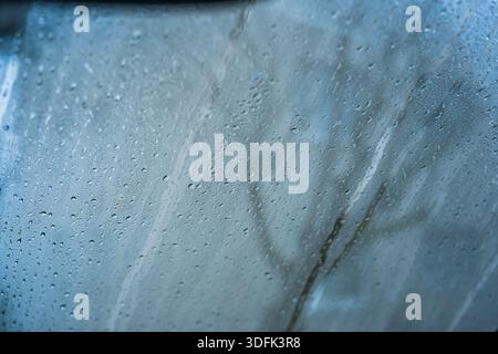 Gouttes de pluie sur une vitre de voiture avec un fond vert flou. Gros plan, faible profondeur de champ, personne Banque D'Images