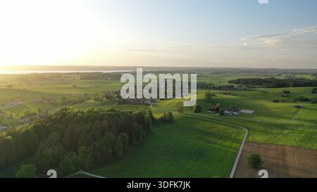 Vue aérienne des villages bavarois idylliques entourés de prairies verdoyantes et de forêts au coucher du soleil avec le lac Starnberg en arrière-plan Banque D'Images