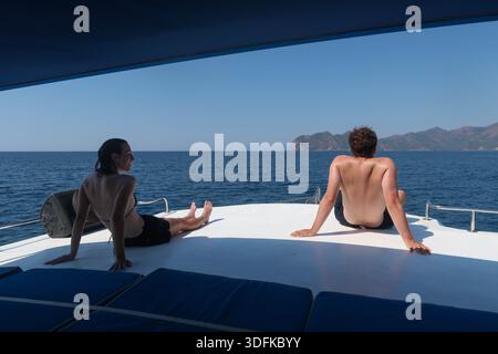 Jeune couple se relaxant sur le pont d'un yacht près de la côte de Dalyan en Turquie, profitant du calme de la mer Méditerranée et des voyages d'été Banque D'Images
