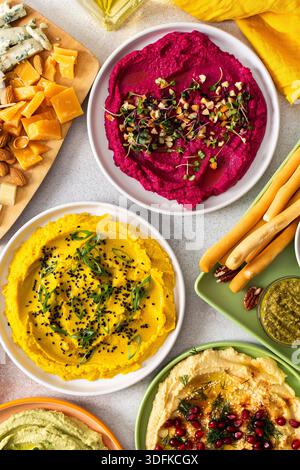 La tartinade colorée comprend des betteraves, des houmous classiques, des brocolis et du curcuma présentés sur un plateau de charcuterie avec des garnitures vibrantes, des gressins et des olives assorties, parfaits pour les rassemblements Banque D'Images
