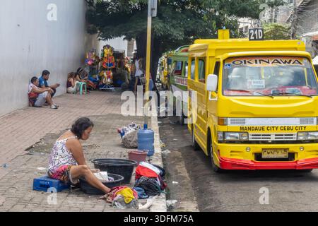 Femme lavant des vêtements dans la rue dans un panier en plastique, Cebu ville, Philippines Banque D'Images
