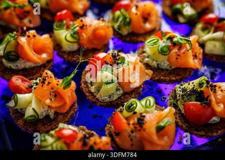 Canapés de saumon élégants surmontés de boucles de concombre et de tomates cerises disposées sur une surface sombre. Banque D'Images