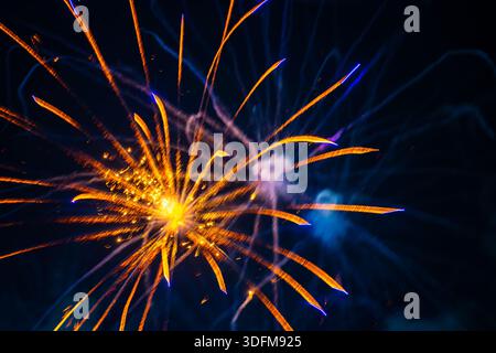 explosion vibrante de feu d'artifice dans le ciel nocturne. Des traînées dorées rayonnent vers l'extérieur à partir d'un centre lumineux. La scène comprend des notes de fumée et de lumière bleue. Banque D'Images