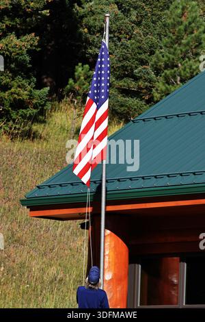 Personne lève un drapeau des États-Unis sur un haut poteau à côté d'un bâtiment de toit vert sur Pikes Peak Highway, Colorado Springs, Colorado, États-Unis, en plein jour. Banque D'Images