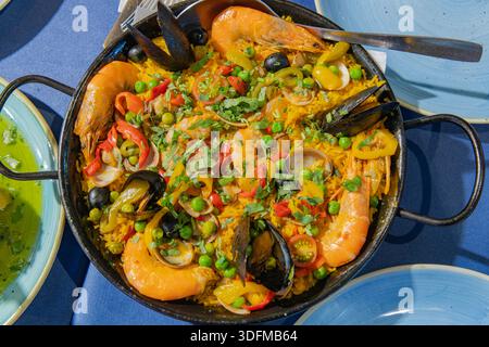 Lisbonne, Portugal - 11 octobre 2025 : une casserole de riz traditionnel aux fruits de mer avec des crevettes et des moules servies sur une table bleue. Banque D'Images
