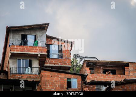 Vue de maisons en briques rouges vibrantes empilées précairement contre le ciel nuageux créent un paysage urbain unique, Comuna 13, Medellin, Colombie. Banque D'Images