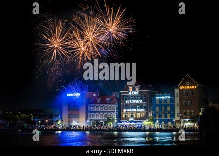 Vue de feux d'artifice vibrants éclairent le ciel nocturne au-dessus des bâtiments colorés reflétés dans l'eau sombre, Willemstad, Curaçao. Banque D'Images