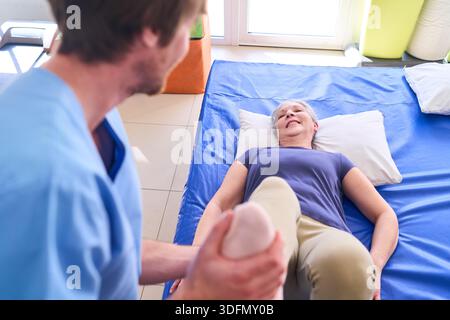 Une femme âgée est allongée pendant un certain temps recevant une physiothérapie des jambes d'un physiothérapeute masculin dans un centre de réadaptation. Cette image peut être utilisée commercialement à illus Banque D'Images