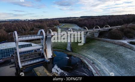 Une vue aérienne de la roue de Falkirk, un ascenseur rotatif pour bateaux, avec un canal, le paysage environnant et des bâtiments lointains sous un ciel nuageux. Banque D'Images