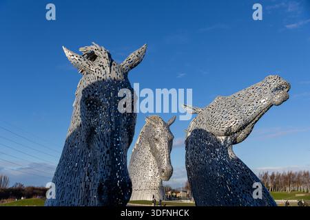 Trois têtes de cheval métalliques monumentales, détaillées avec des motifs complexes, dominent le premier plan dans un ciel bleu clair. Banque D'Images