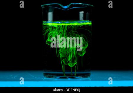 Dissolution et étalement d'une substance verte dans un flacon avec un liquide clair. Réaction chimique observée en laboratoire. Copyspace. Banque D'Images