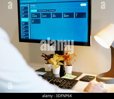 Médecin masculin d'âge moyen au bureau à domicile examine le tableau de bord du DME du patient avec des notes assistées par IA, des paramètres vitaux, des laboratoires et des résumés de visite sur le concept de moniteur Banque D'Images