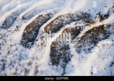 Vue macro d'un sol enneigé avec des rainures de chenilles sombres et du gravillonnage de la route, un arrière-plan détaillé de texture hivernale montrant de la neige comprimée, de la saleté et des marques de sculpture Banque D'Images