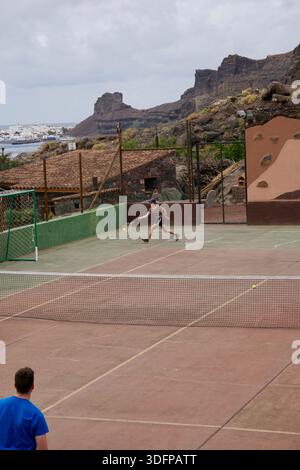 Deux hommes jouant au tennis sur un court extérieur à Gran Canaria, îles Canaries, Espagne, entouré de palmiers et de paysages volcaniques Banque D'Images