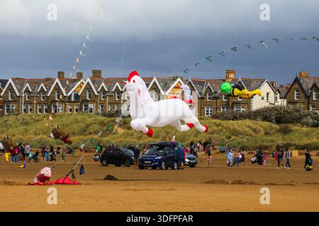 Cerf-volant gonflable géant volant au-dessus de la plage lors d'un festival de cerf-volant à Lytham St Annes, avec spectateurs et véhicules sur le sable. Banque D'Images
