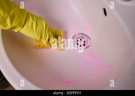 Propriétaire prépare la baignoire soigneusement, gros plan de l'écume de savon de nettoyage des mains du drain de la baignoire, vue détaillée de la personne désinfectant la baignoire avec de la mousse rose Banque D'Images