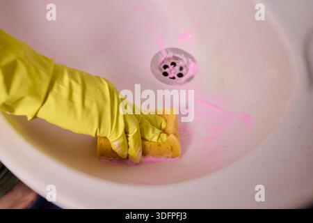 Propriétaire prépare la baignoire soigneusement, gros plan de l'écume de savon de nettoyage des mains du drain de la baignoire, vue détaillée de la personne désinfectant la baignoire avec de la mousse rose Banque D'Images
