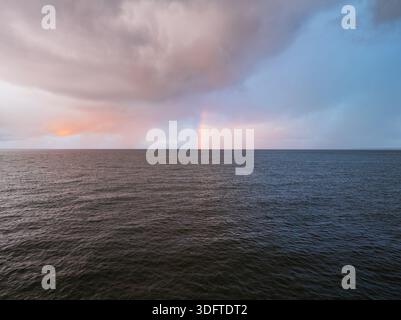 Vue aérienne par drone d'un arc-en-ciel spectaculaire au-dessus de l'horizon de la mer Baltique en Estonie sous des nuages d'orage morose au coucher du soleil. Banque D'Images