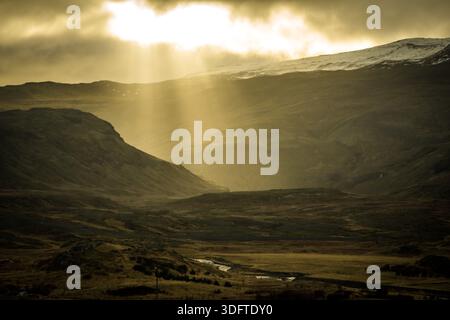 Vue des rayons de soleil perçant à travers les nuages spectaculaires sur le paysage accidenté et vallonné, projetant une lueur éthérée à travers le fond de la vallée, Grundar Banque D'Images