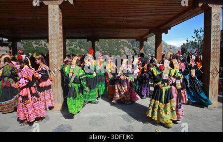 Kalash, Pakistan - 24 décembre 2025 : vue de femmes Kalash, ornées de robes traditionnelles vives, dansent sous la verrière en bois sur fond de R Banque D'Images