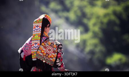 Kalash, Pakistan - 24 décembre 2025 : vue d'une femme Kalash, ornée d'une tenue traditionnelle vibrante, debout sur fond de collines verdoyantes. Banque D'Images