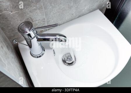 Un robinet d'eau chromé au design moderne qui coule dans un évier en céramique blanche. Vue de dessus. Banque D'Images