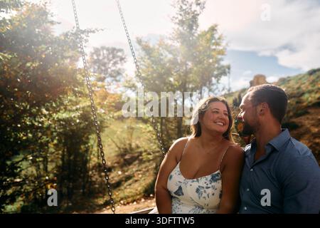 Couple romantique assis sur une balançoire en plein air pendant Golden Hour - rétroéclairé Portrait of Love and Connection Banque D'Images