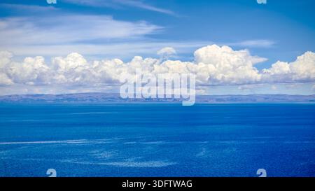 Vue de l'eau bleu profond rencontrant le rivage lointain sous un ciel lumineux rempli de nuages blancs gonflés, scintillant dans la lumière du soleil, Taquile Island, Pérou. Banque D'Images