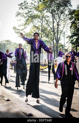 Mexico, Mexique - 04 novembre 2023 : vue de marcheurs sur pilotis dans des costumes violets et noirs vibrants, une procession animée le long du défilé. Banque D'Images