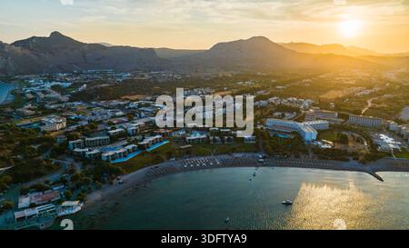 Vue aérienne de la lumière dorée du soleil embrassant la baie tranquille et la plage de sable, contrastant avec les montagnes escarpées, Rhodes, Grèce. Banque D'Images