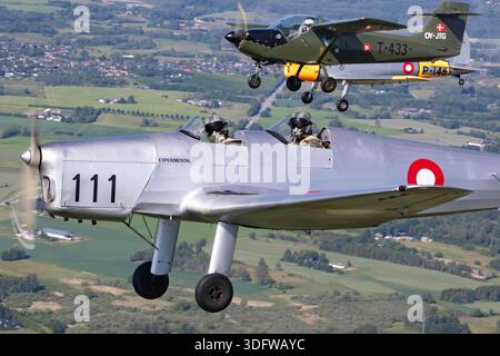 Image en gros plan air-air montrant les pilotes de trois avions anciens volant en formation serrée à Danish Airpower 2025. On peut voir le de Havilland Canada DHC-1 Chipmunk 22 avec son moteur à pistons en ligne et son cockpit tandem, le Saab MFI-15 Safari équipé d'un moteur à pistons Lycoming quatre cylindres, et le SAI KZ II Sport, un modèle danois à ailes basses avec une configuration à pistons. La photographie met l'accent sur le vol contrôlé en formation, les auvents des aéronefs et les conditions de vol opérationnelles. Banque D'Images