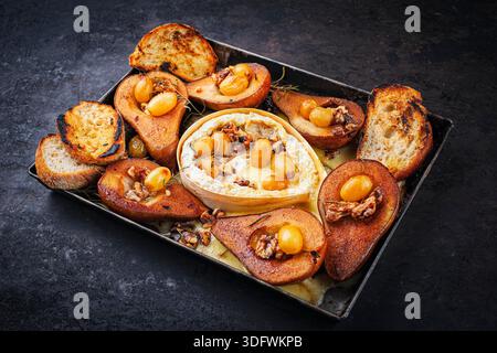 camembert cuit au four avec poires glacées caramélisées, noix et raisins et baguette servie sur une assiette en métal rustique Banque D'Images