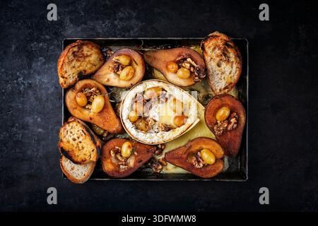 camembert cuit au four avec poires glacées caramélisées, noix et raisins et baguette servie sur une assiette en métal rustique Banque D'Images