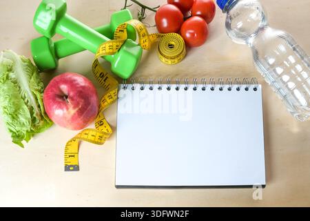Cahier à anneaux vierges et bases de fitness telles que pomme, légumes, bouteille d'eau et haltères, maquette pour une liste d'objectifs, minceur et une vie saine Banque D'Images