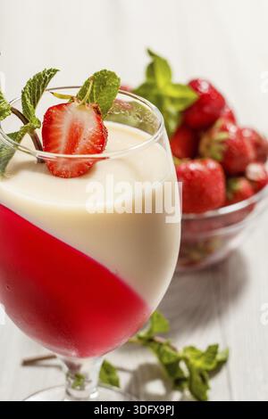 Gelée de cerises et le lait dans le verre décoré de feuilles de menthe et fraise morceau avec les fraises au bol en verre sur l'arrière-plan Banque D'Images