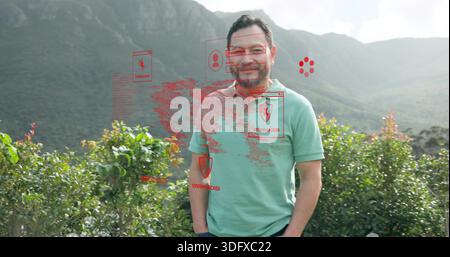 Homme debout dans un polo vert clair et un pantalon sombre parmi les arbustes, montrant des boucliers PIRATÉS PAR LE SYSTÈME rouge Banque D'Images