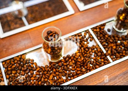 Grains de café torréfiés renversés dans des tasses en verre sur le comptoir. Banque D'Images