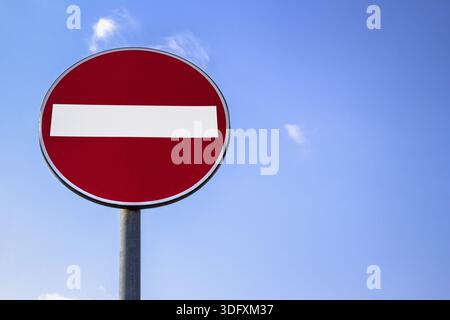 Un panneau circulaire rouge avec une barre blanche indiquant « PAS D'ENTRÉE » sur un poteau en métal gris contre un ciel nuageux bleu Banque D'Images