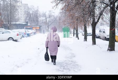 Une femme vêtue d'un manteau d'hiver rose descend un trottoir enneigé de la ville lors d'une forte chute de neige. Banque D'Images