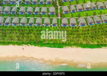Maisons côte avec cocotiers et sable blanc dans l'eau Azur cristal. Vue aérienne de dessus de nombreux bâtiments en ligne identiques avec des jardins densément construits Banque D'Images