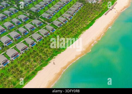 Maisons côte avec cocotiers et sable blanc dans l'eau Azur cristal. Vue aérienne de dessus de nombreux bâtiments en ligne identiques avec des jardins densément construits Banque D'Images