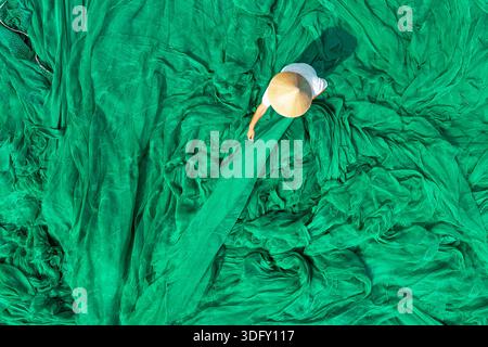 Vue aérienne de dessus mâle gars dans le chapeau authentique traditionnel vietnamien démêler les filets de pêche verts se préparant pour la pêche et sortir en mer. Banque D'Images