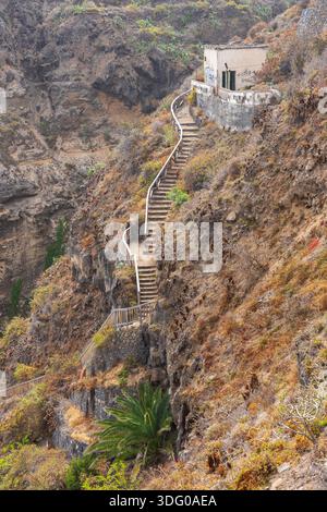 Escalier escarpé à flanc de falaise avec des garde-corps en bois menant à un petit bâtiment abandonné sur une pente volcanique accidentée à Rambla de Castro, Tenerife, Canary Isla Banque D'Images