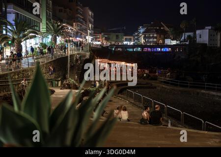 PUERTO DE LA CRUZ, TENERIFE, ESPAGNE - 9 AOÛT 2025 : promenade bondée au bord de l'eau avec restaurants et gens la nuit près de la côte rocheuse. Banque D'Images