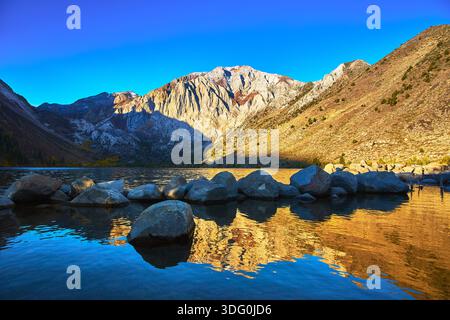 Mountain Lake Sunrise Reflection avec Rocky Shore et Peaks Banque D'Images