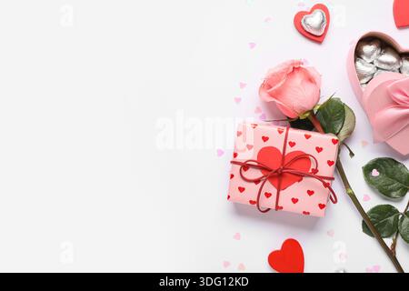 Boîtes cadeaux avec bonbons, coeurs décoratifs et fleur de rose sur fond blanc. Célébration de la Saint-Valentin Banque D'Images