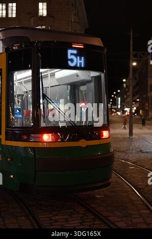 Un tramway moderne s'arrête dans une rue calme de la ville la nuit, son affichage lumineux de l'itinéraire et les lumières brillantes se reflétant sur le verre et les rails, créant un Banque D'Images
