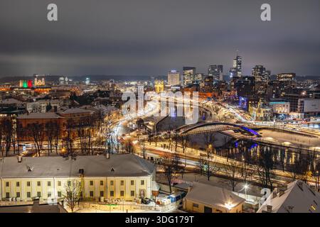 Une vue nocturne hivernale de Vilnius montrant un paysage urbain lumineux le long de la rivière Neris, avec des ponts illuminés, un trafic fluide Banque D'Images