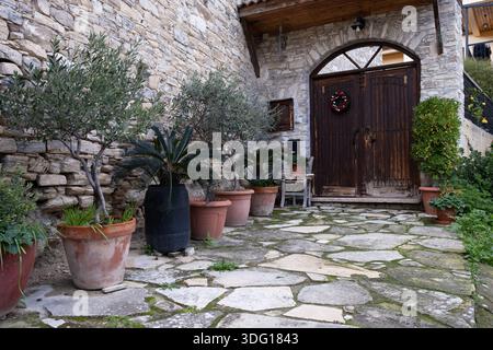 Bâtiment traditionnel en pierre avec une porte en bois altérée, une couronne de noël et des plantes en pot sur un chemin de dalles. Village de Lefkara Chypre Banque D'Images